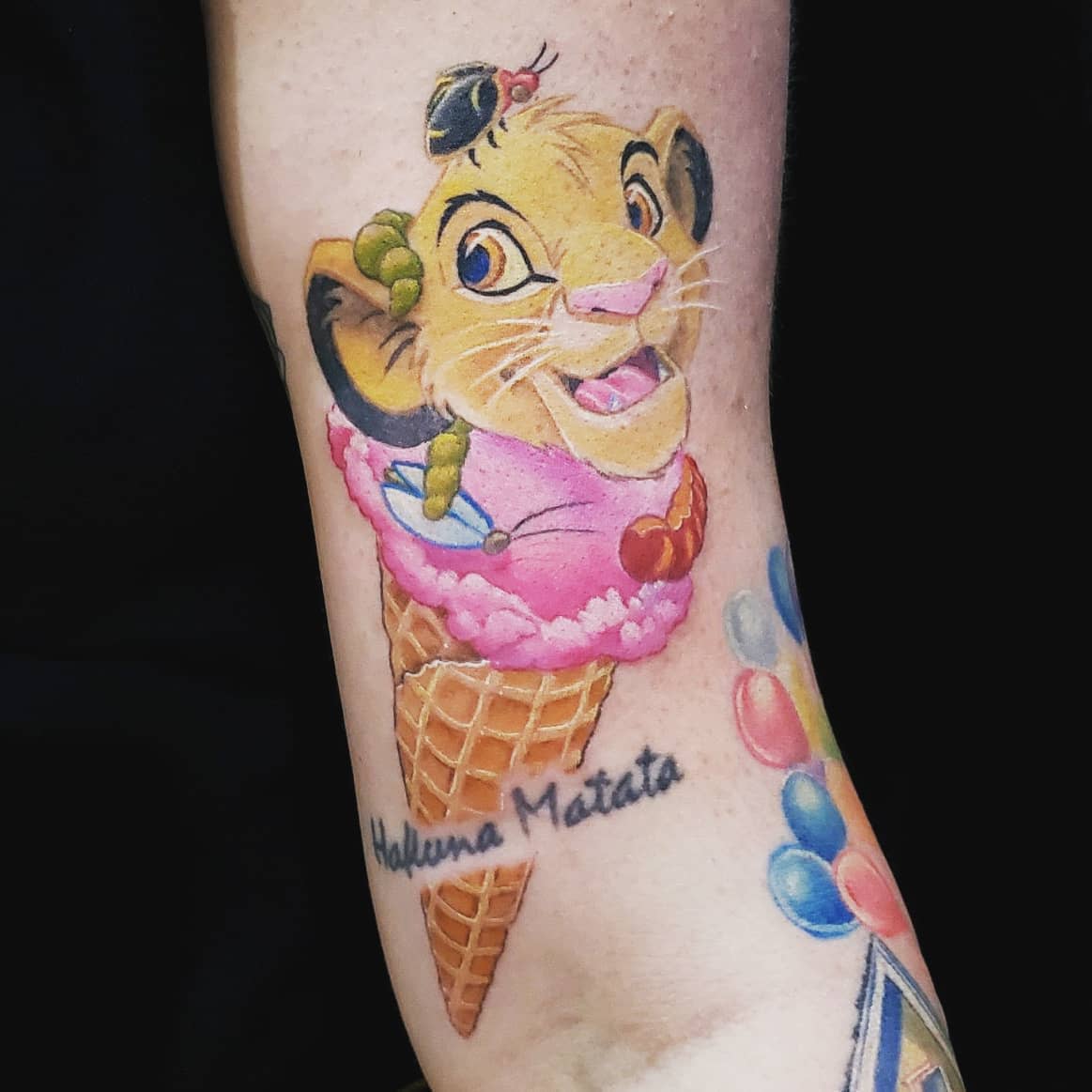 Tattoo of a lion cub Simba in an ice cream cone with "Hakuna Matata" text